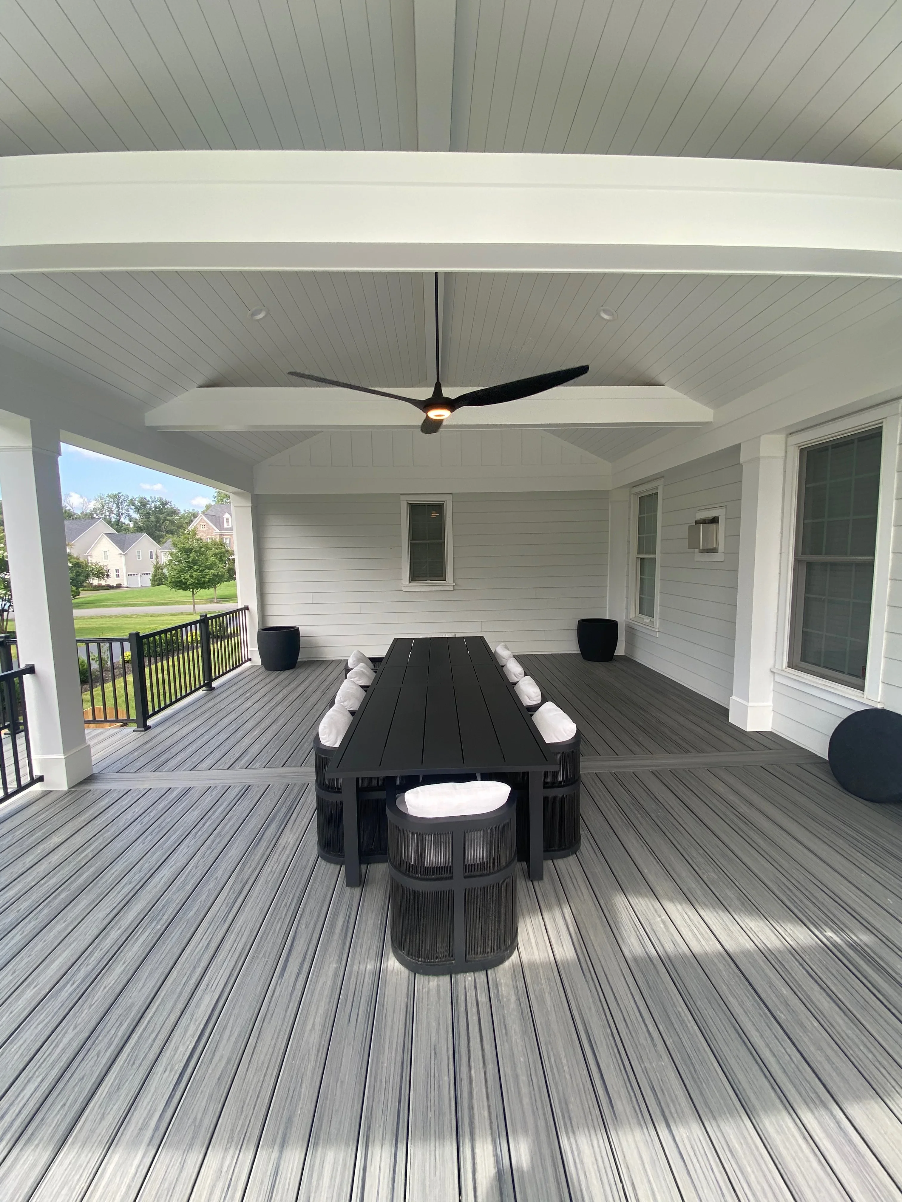 Gray composite deck with white covered patio, black dining table, and ceiling fan