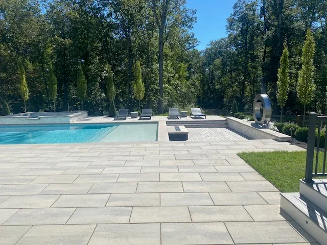 Gray stone paver patio surrounding pool with spa feature and lounge chairs
